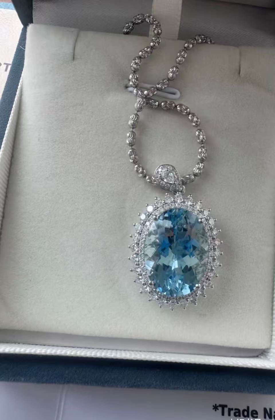 Oval aquamarine double-halo pendant on a woven silver chain in an ivory gift box