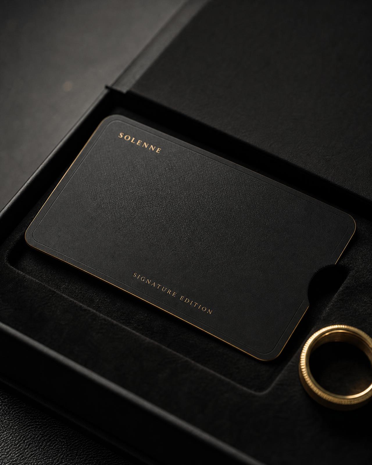 Signature Edition matte black titanium card with gilt engraved border, half lifted from a black box