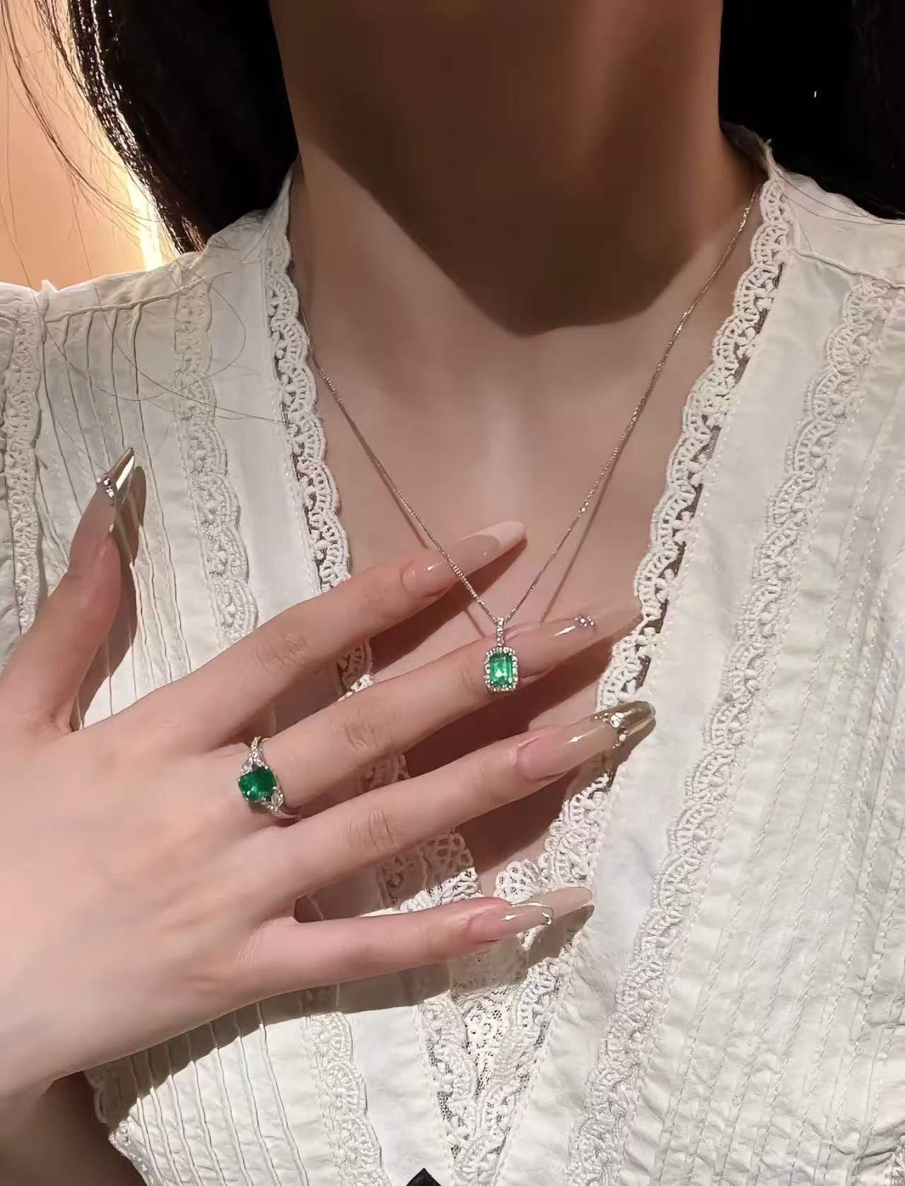 Model wearing an emerald-cut green pendant with a matching green stone ring