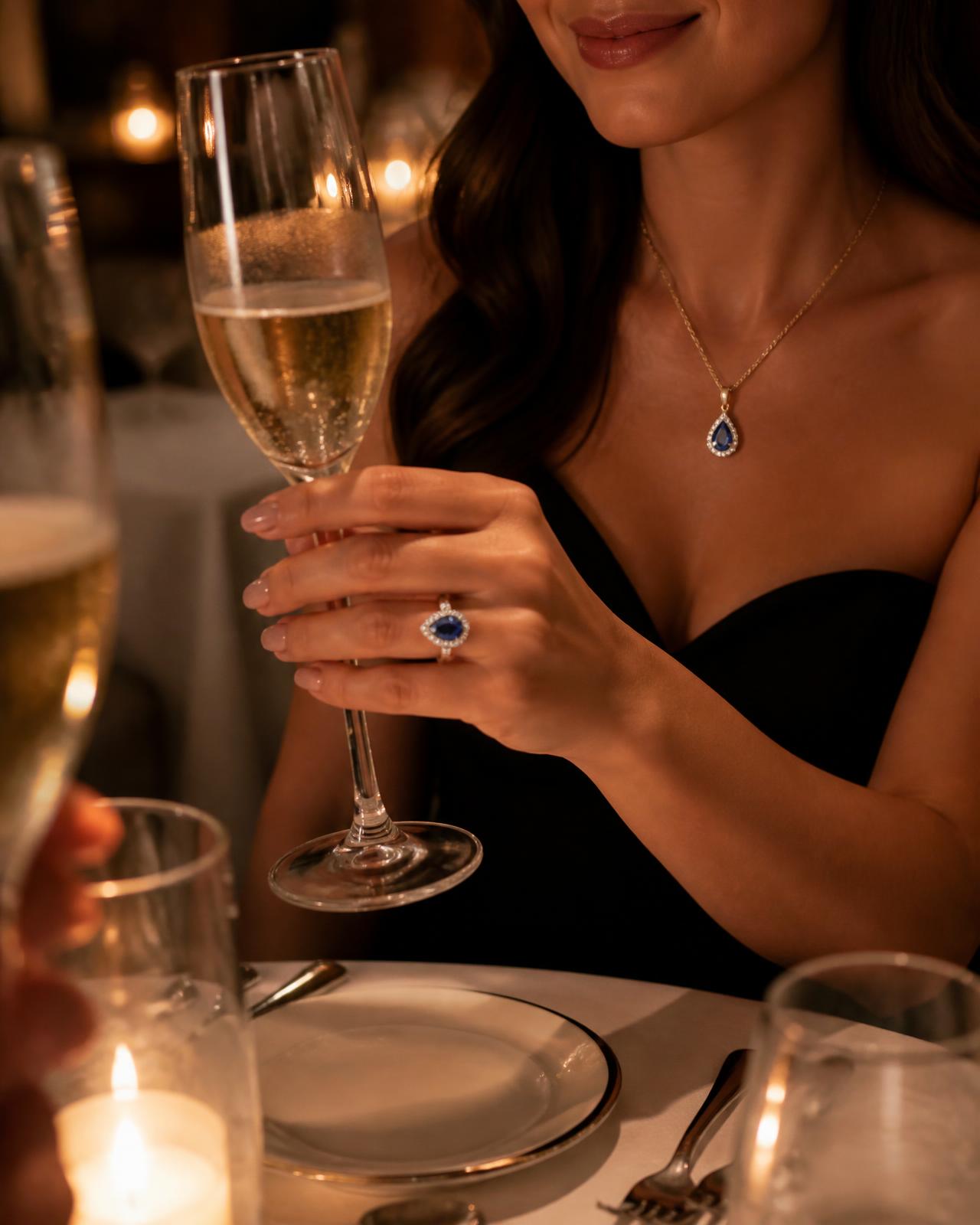 A woman raising a champagne glass wearing a sapphire halo pendant and ring
